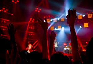 Disco party concert with large group of happy dancing people, silhouette of hands up in the air over blur red colorful stage lights, active lifestyle entertainment, music nightclub, night life concept